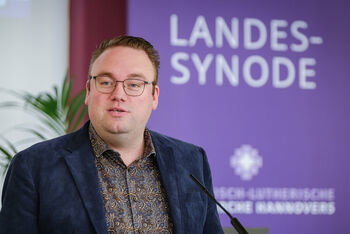 Eine männlich lesbare Person an einem Rednerpult