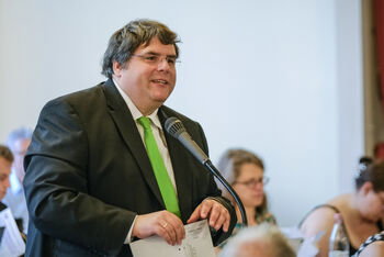 Eine männlich lesbare Person an einem Mikrofon