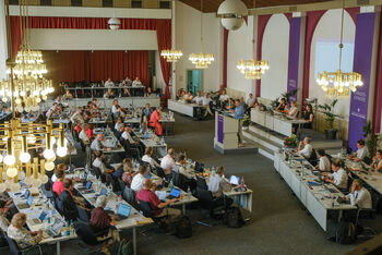 Viele Personen an Tischen in einem Sitzungssaal