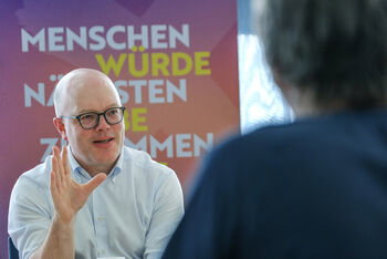 Eine männlich lesbare Person vor einem Roll-up