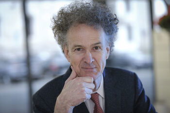 Ein mittelalter Mann mit üppiger Frisur stützt sein Kinn auf die Hand.