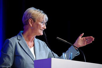 Eine weiblich gelesene Person mit blauem Blazer an einem Mikro.