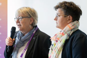 Zwei weiblich gelesene Personen mit einem Mikro.