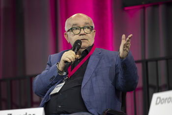 Eine als Mann gelesene Person mit Brille und hoher Stirn spricht in ein Mikrofon.