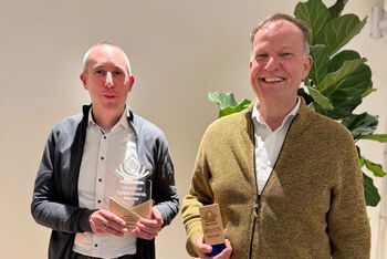 Zwei als Männer lesbare Personen mit Trophäen in der Hand.