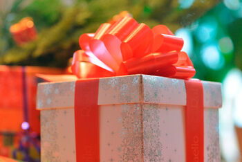 Ein weiß-silberner Karton mit roter Schleife vor einem Weihnachtsbaum.