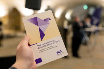 Eine Hand hält ein Buch mit der Aufschrift „Welt in Unordnung – Gerechter Friede im Blick“
