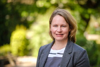 Portraitfoto einer als Frau lesbaren Person vor einem grünen Hintergrund