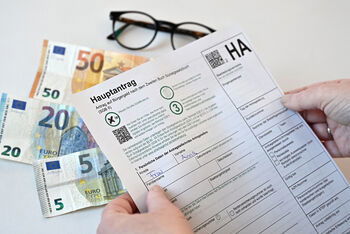 Ein Antrag auf Bürgergeld, im Hintergrund liegen Geldscheine