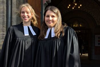 Zwei Frauen im Talar vor einer Kirche.