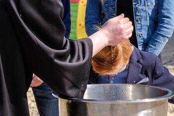 Eine Hand träufelt einem Täufling Wasser über den Kopf