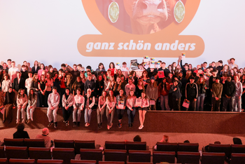 Viele junge Menschen stehen vor einer großen Kinoleinwand.