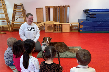 Ein Hund liegt auf einer Matte neben Kindern und einer erwachsenen Person.