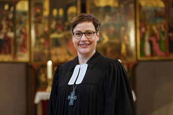 Eine als Frau lesbare Person im Talar und mit Bischofskreuz steht in einer Kirche.