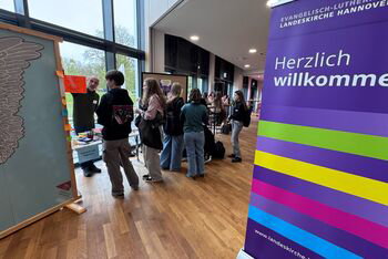 Mehrere junge Menschen stehen an einem Infostand, umrahmt von Rollups.