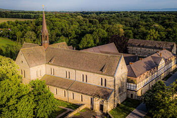 Eine große historische Kirche mit angrenzenden Fachwerkgebäuden inmitten mehrerer Bäume.