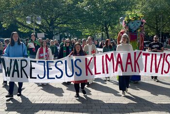 Menschen auf einer Demonstration, sie halten ein Banner, auf dem steht "Wäre Jesus Klimaaktivist?".