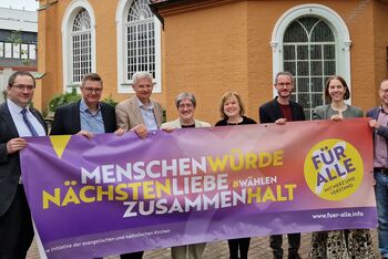 Mehrere als Frauen und Männer lesbare Personen halten ein Banner mit den Worten Menschenwürde, Nächstenliebe, Zusammenhalt