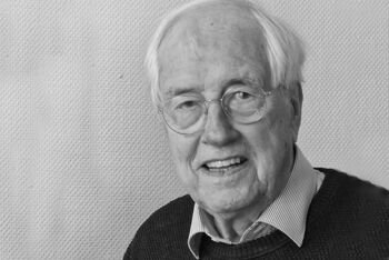 Schwarzweiß-Portrait von einer als Mann lesbaren Person mit Brille und grauem Haar.