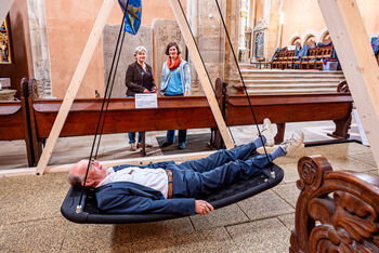 Eine als Mann lesbare Person in einer Schaukel in einer Kirche