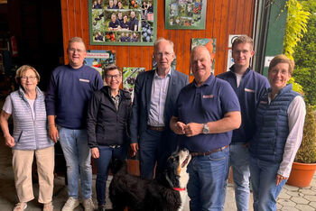 Mehrere als Männer und Frauen lesbare Personen und ein Hund auf einem Hof.