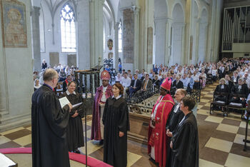 Mehrere Menschen im geistlichen Gewand stehen im Altarraum einer vollbesetzten Kirche.