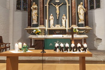 Ein Tisch mit mehreren Kerzen mit Trauerflor vor einem Altar