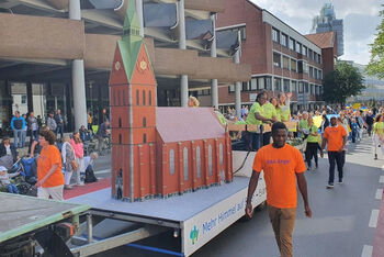 Mehrere Menschen ziehen mit einem Kirchenmodell auf einem Anhänger durch die Straße.