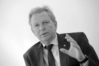 Schwarz-weiß-Bild einer als Mann lesbaren Person, die mit erhobener Hand spricht.