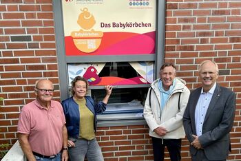 Vier Menschen stehen vor einem „Babykörbchen“ für Mütter in Not