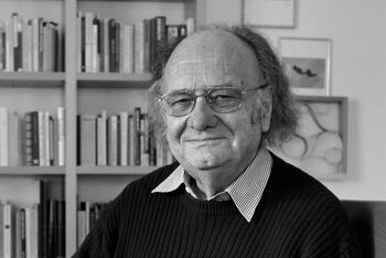 Eine männlich gelesene Person mit Brille und längerem grauen Haar. 