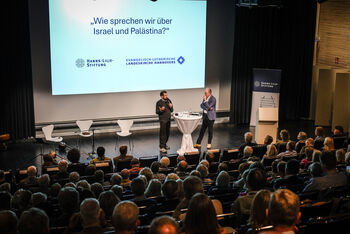 Zwei Menschen diskutieren auf einer Bühne vor Publikum