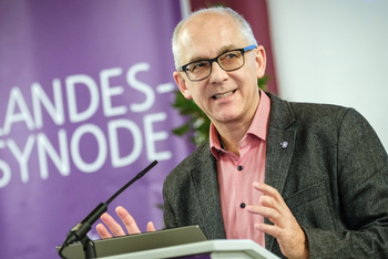 Eine männlich lesbare Person steht an einem Rednerpult und spricht.