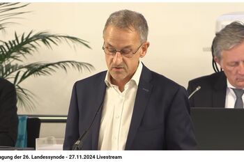 Eine männlich gelesene Person mit kurzem haar in weißem Hemd und Sakko.