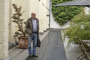 Eine als Mann lesbare Person im Innenhof eines Hotels.