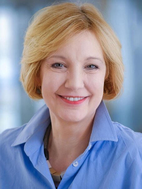 Eine weiblich lesbare Person im Portrait mit kinnlangem blondem Haar und einer blauen Bluse. 