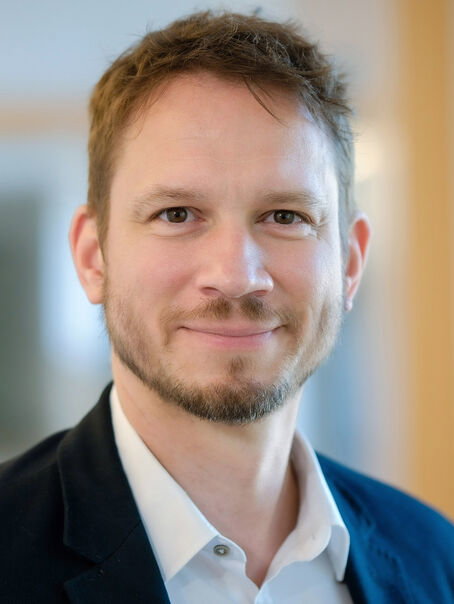 Eine männlich gelesene Person mit kurzen braunen Haaren und Vollbart. 