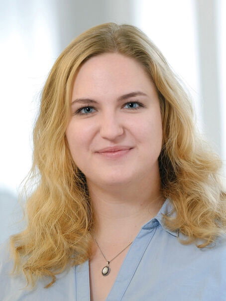 Eine weiblich gelesene Person mit schulterlangem blonden Haar und einer hellblauen Bluse. 