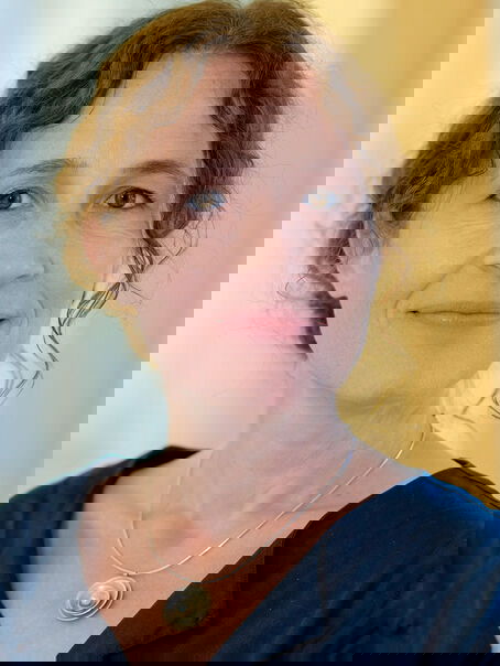Das Bild zeigt eine weiblich lesbare Person mit längeren, hochgesteckten dunklen Haaren und einem dunklen Oberteil.