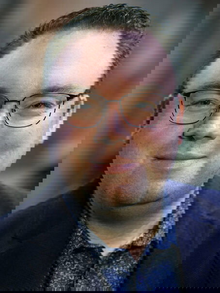 Eine männlich zu lesende Person mit Brille schaut in die Kamera.