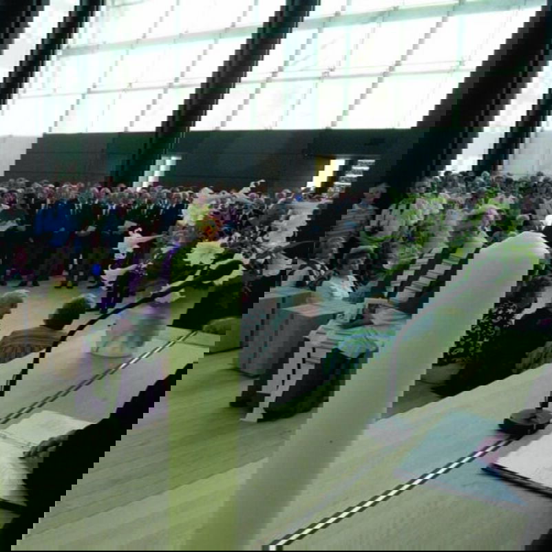 Das Bild zeigt eine weiblich lesbare Person, die in einem hellen modernen Gebäude am Altar steht und mit vielen Menschen Gottesdienst feiert.