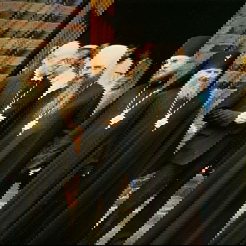 Das Bild zeigt einen Gruppe von männlich lesbaren Personen, einige davon in kirchlichen Gewändern, vor dem Eingang einer Kirche.