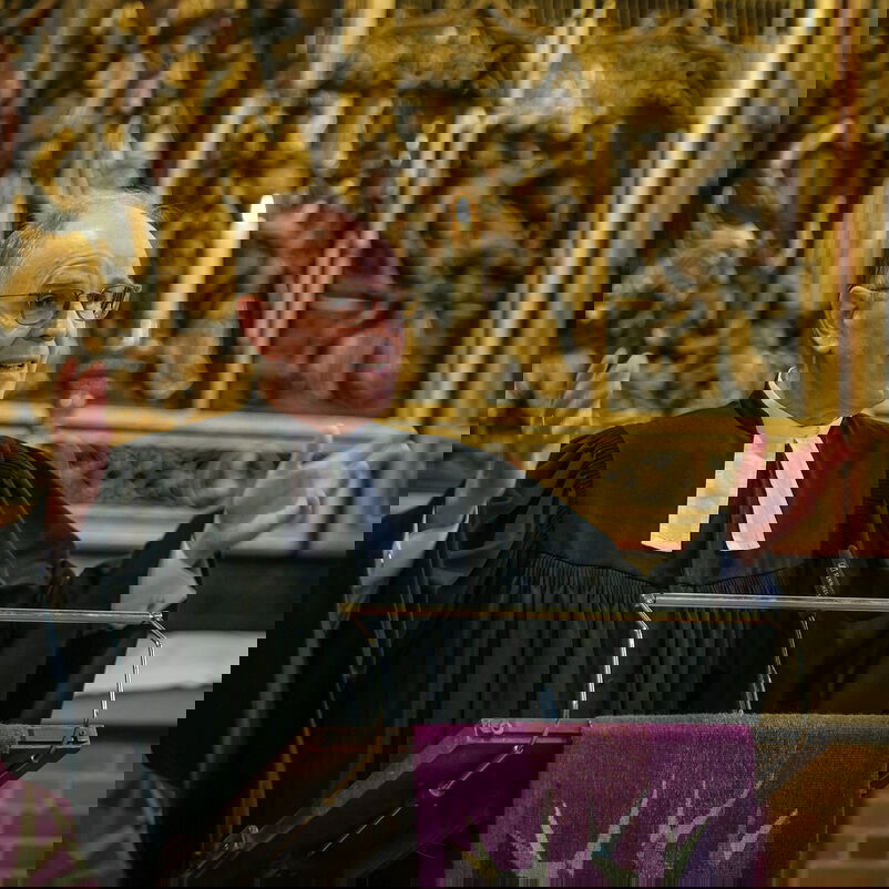 Eine männlich lesbare Person steht an einem Lesepult vor einem Altar