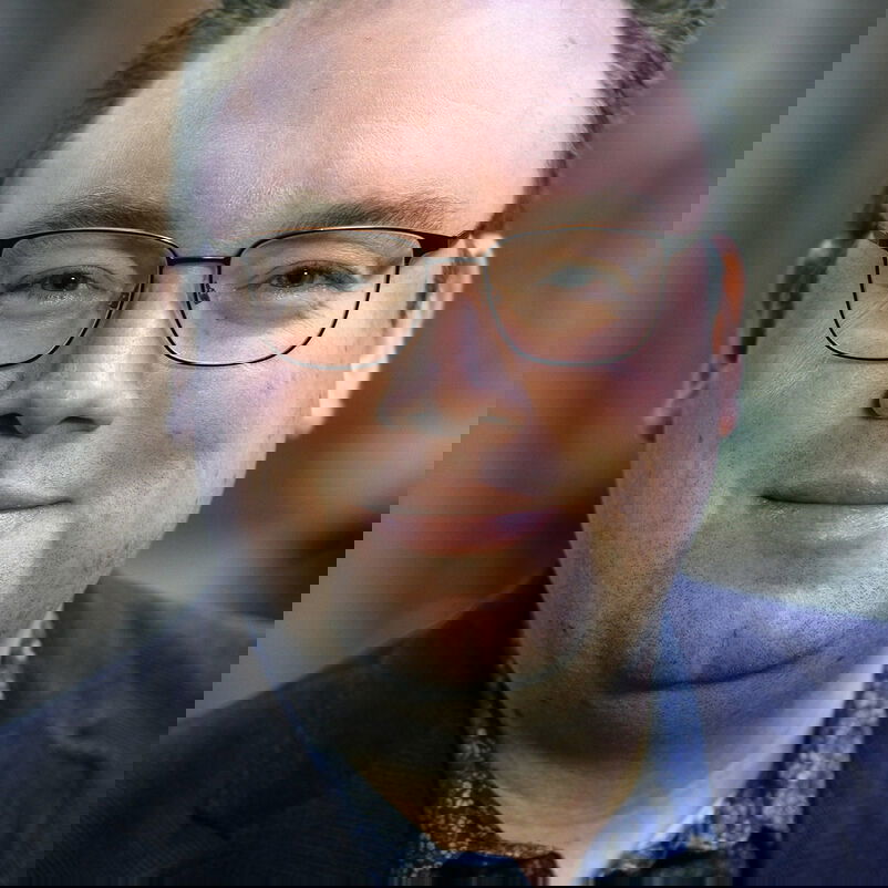 Eine männlich zu lesende Person mit Brille schaut in die Kamera.