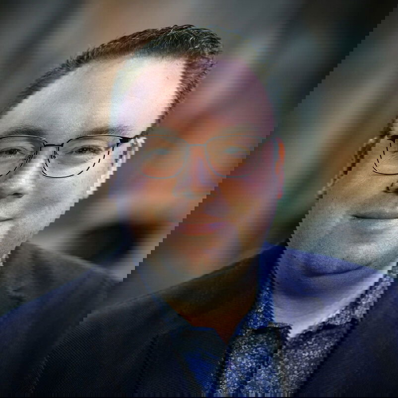 Eine männlich zu lesende Person mit Brille schaut in die Kamera.