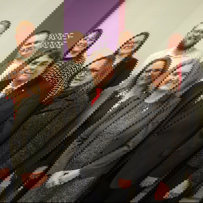 Sechs weiblich und vier männlich zu lesende Personen stehen als Gruppe zusammen und schauen in die Kamera.