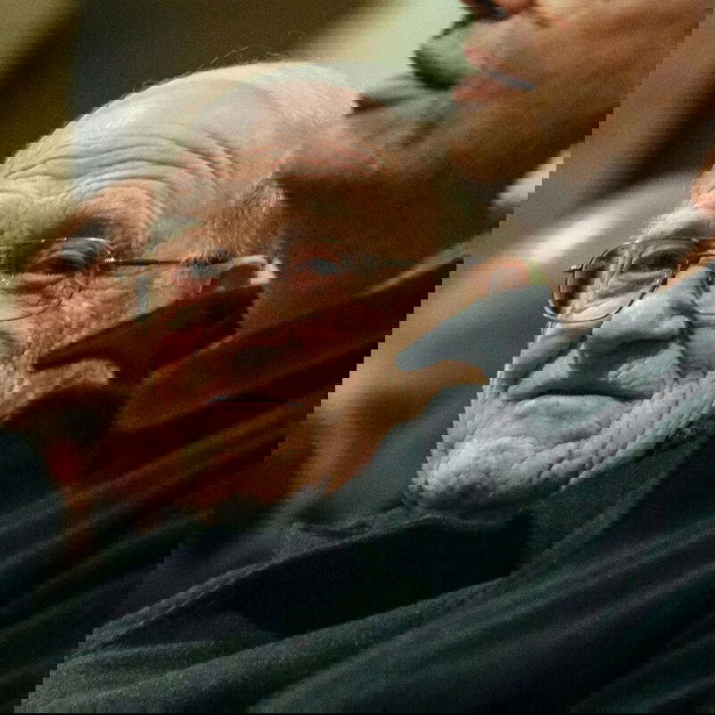 Eine männlich lesbare Person mit weißen Haaren und Brille. 