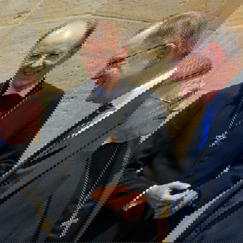 Drei männlich lesbare Personen, zwei davon in schwarzem Talar, eine im blauen Anzug; alle lachend im Gespräch.