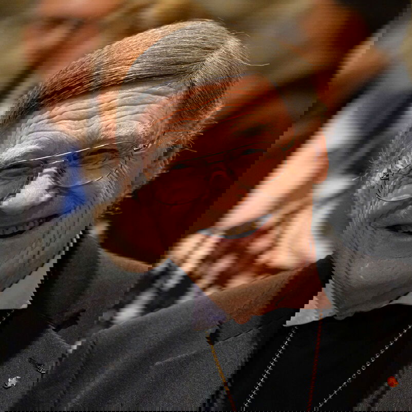 Eine männlich lesbare Person mit grauem Haar und Brille, lachend.