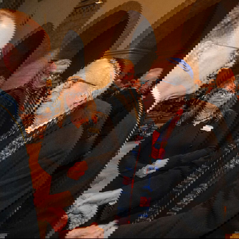 Zwei Männer, einer mit Kippah, begrüßen sich. Im Hintergrund stehen weitere Personen in einem Kirchenschiff.